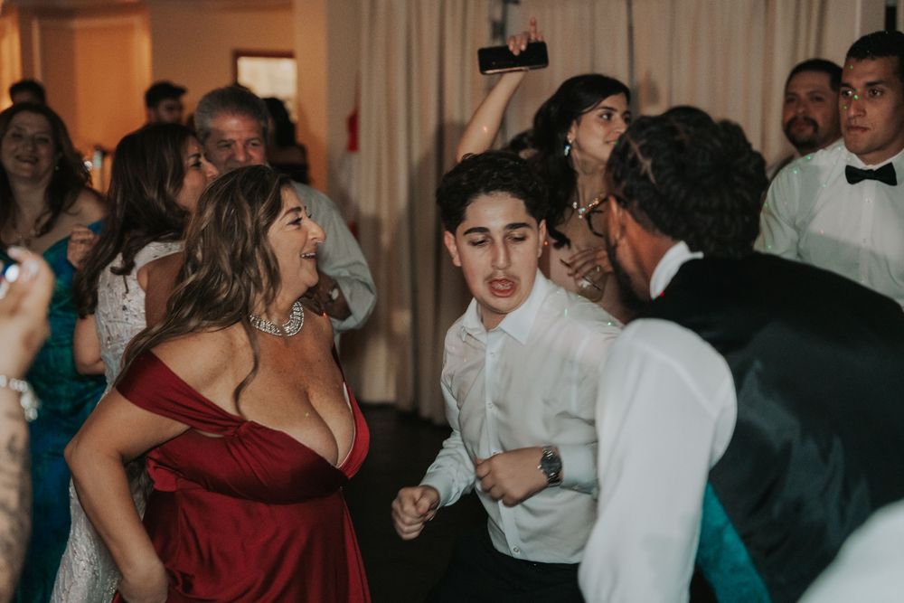 Wedding guests dance and socialize on a crowded dance floor at an evening reception.