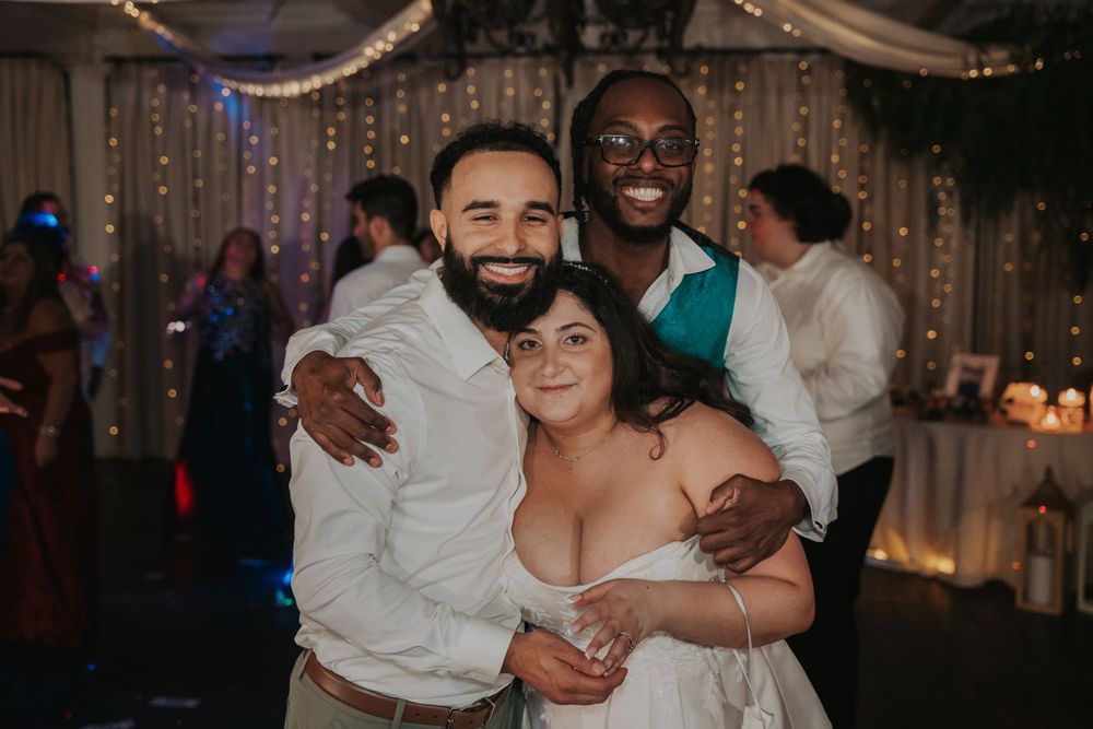 Wedding reception guests dancing and embracing on a dimly lit dance floor with string lights in the background.