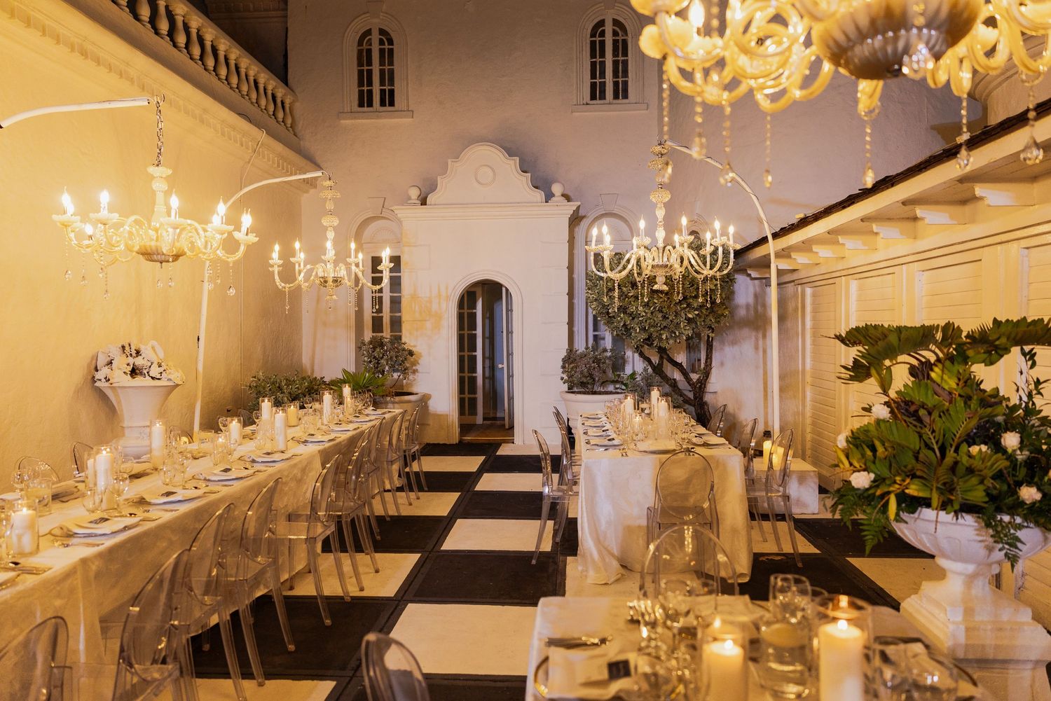 An elegant white wedding reception venue with crystal chandeliers and tables set for a formal celebration.
