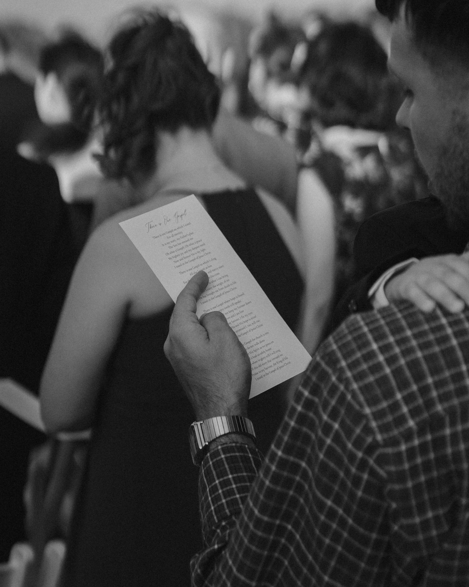 A guest holds a wedding program while attending a formal ceremony in black and white.