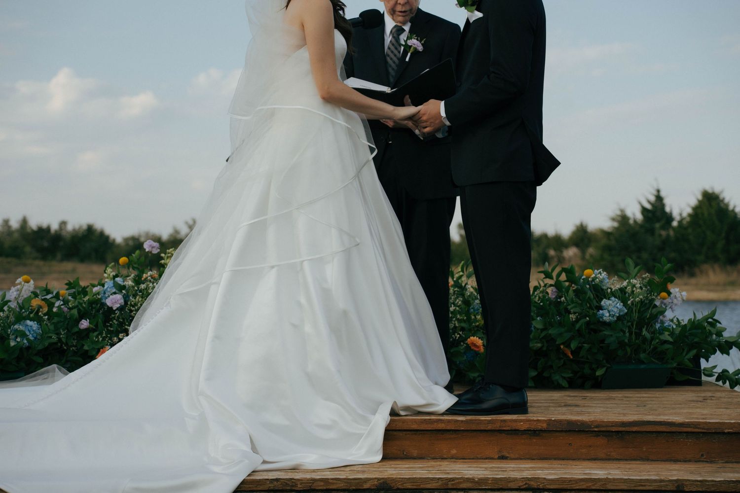 A wedding couple stands together outdoors during their ceremony while a person officiates their marriage.