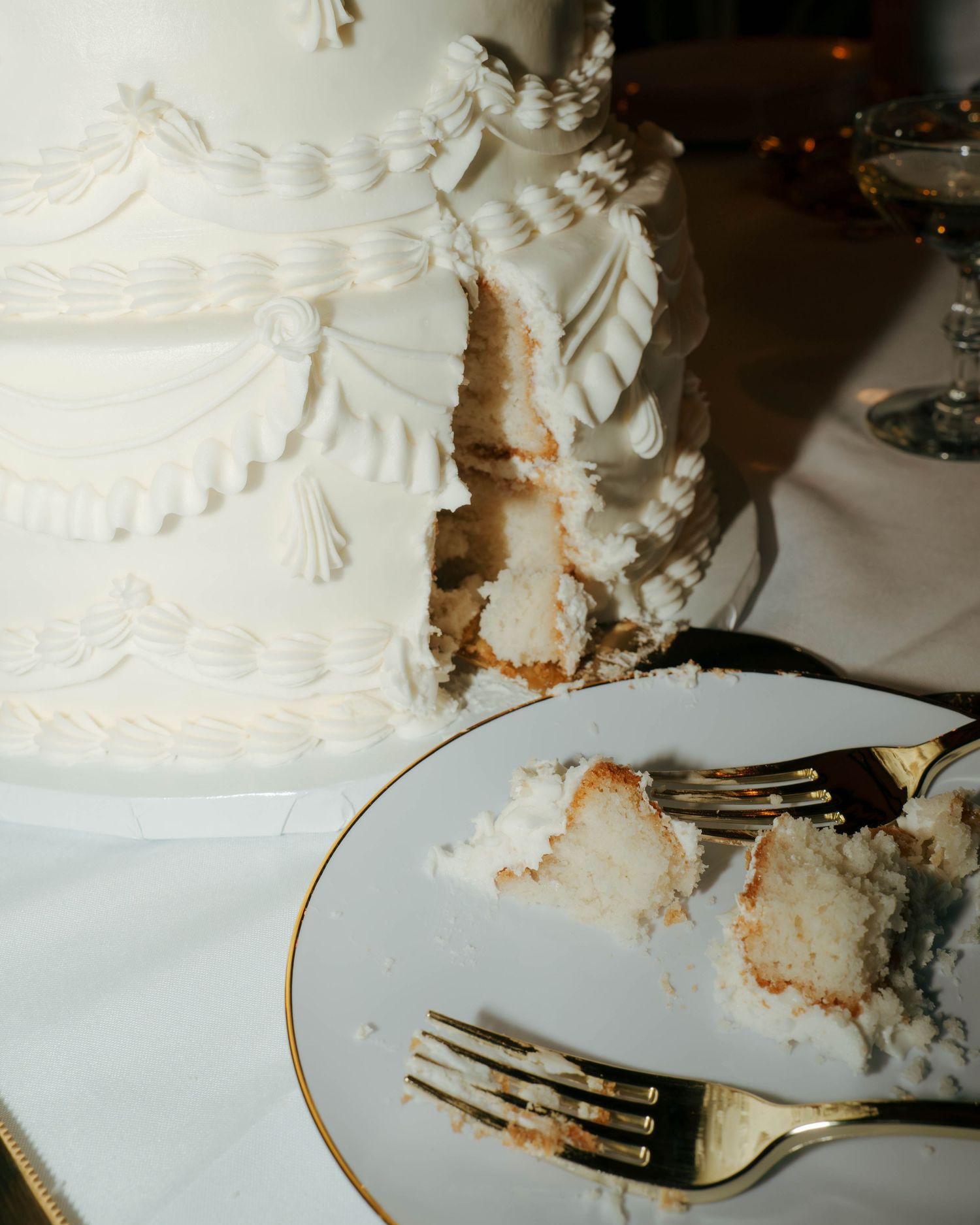 A sliced white wedding cake with elegant piped frosting details and forks on a plate.
