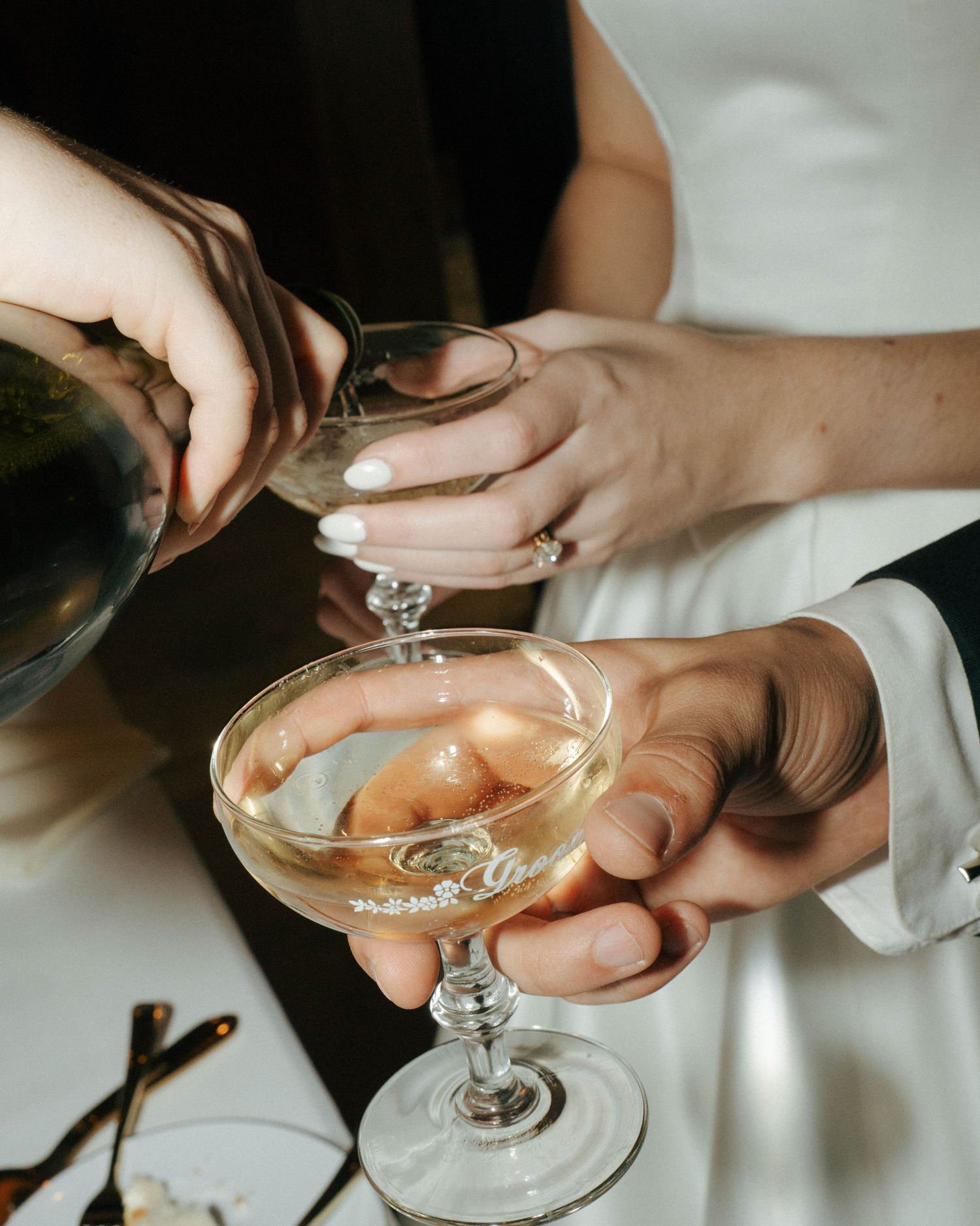 Hands holding a champagne coupe glass filled with a pink cocktail against a light background.
