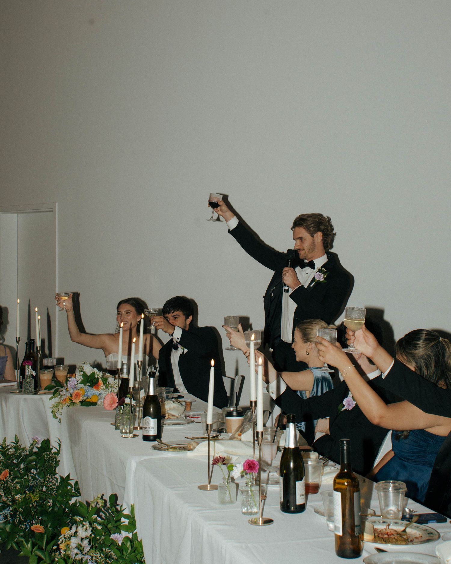 Wedding guests raising glasses in a toast during a reception dinner at a decorated banquet table.