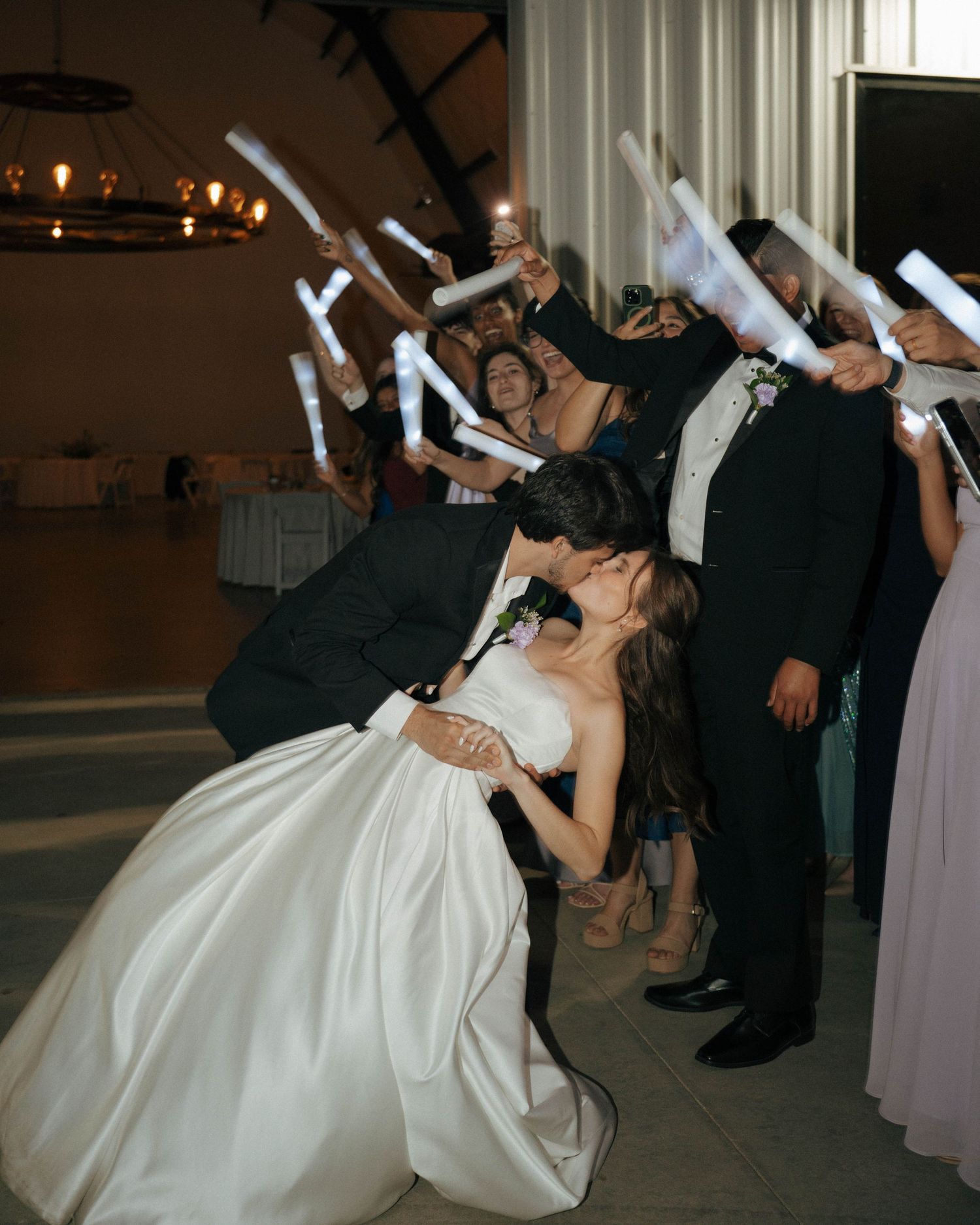 Wedding guests hold light-up foam sticks while celebrating during a reception dance.