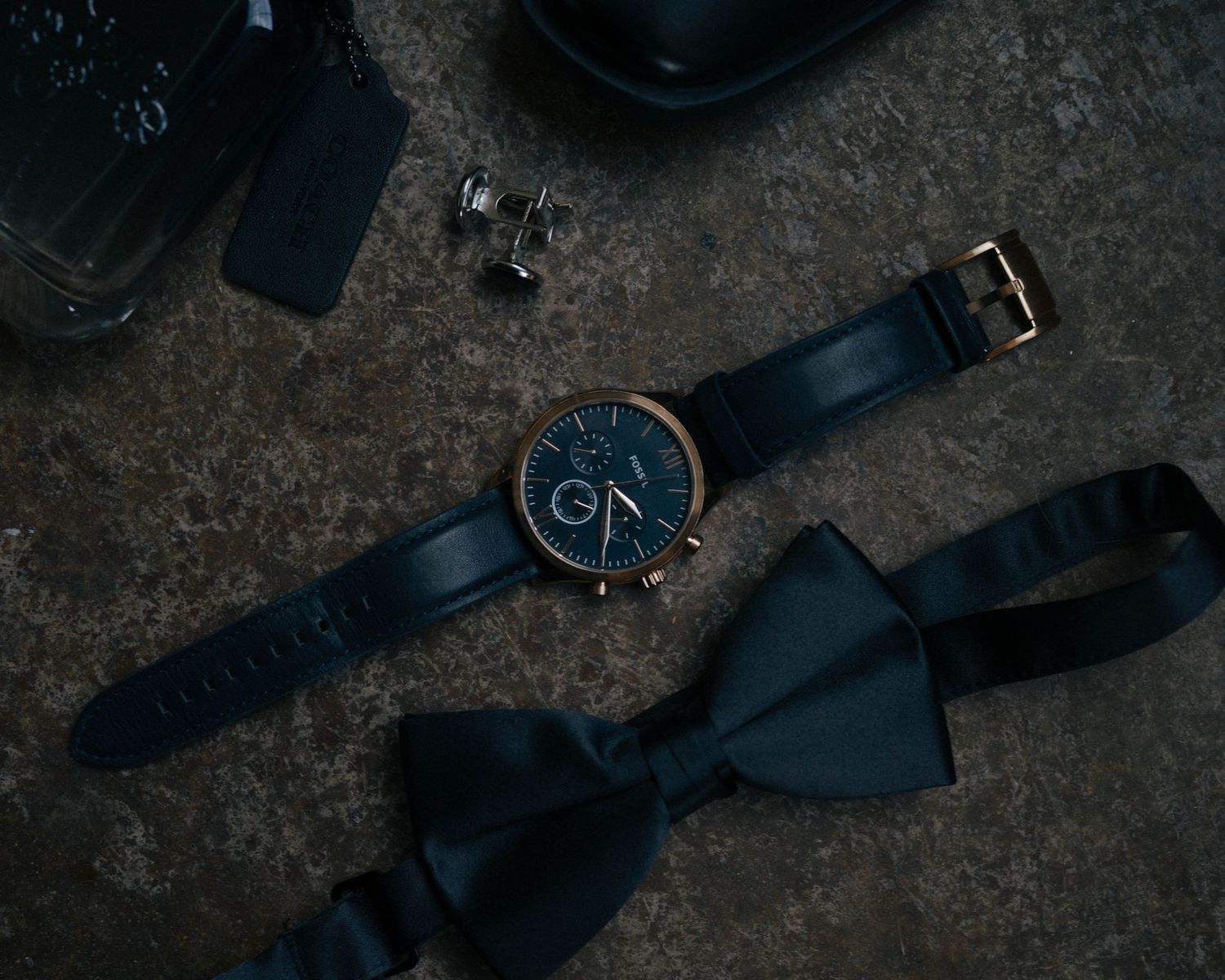 A black leather belt with a silver buckle lies coiled on a dark textured surface.