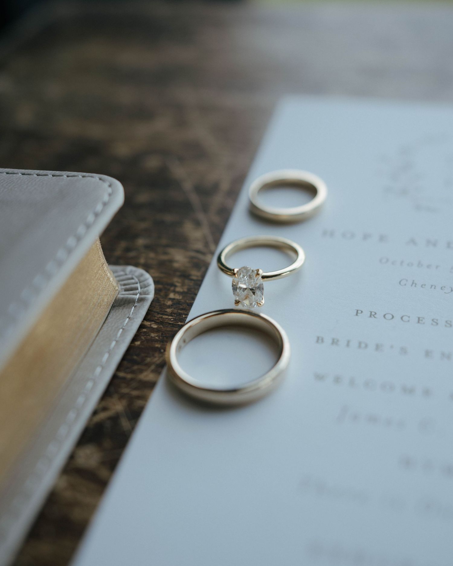 Close-up shots of wedding rings and a bride's guide book on a rustic wooden surface.
