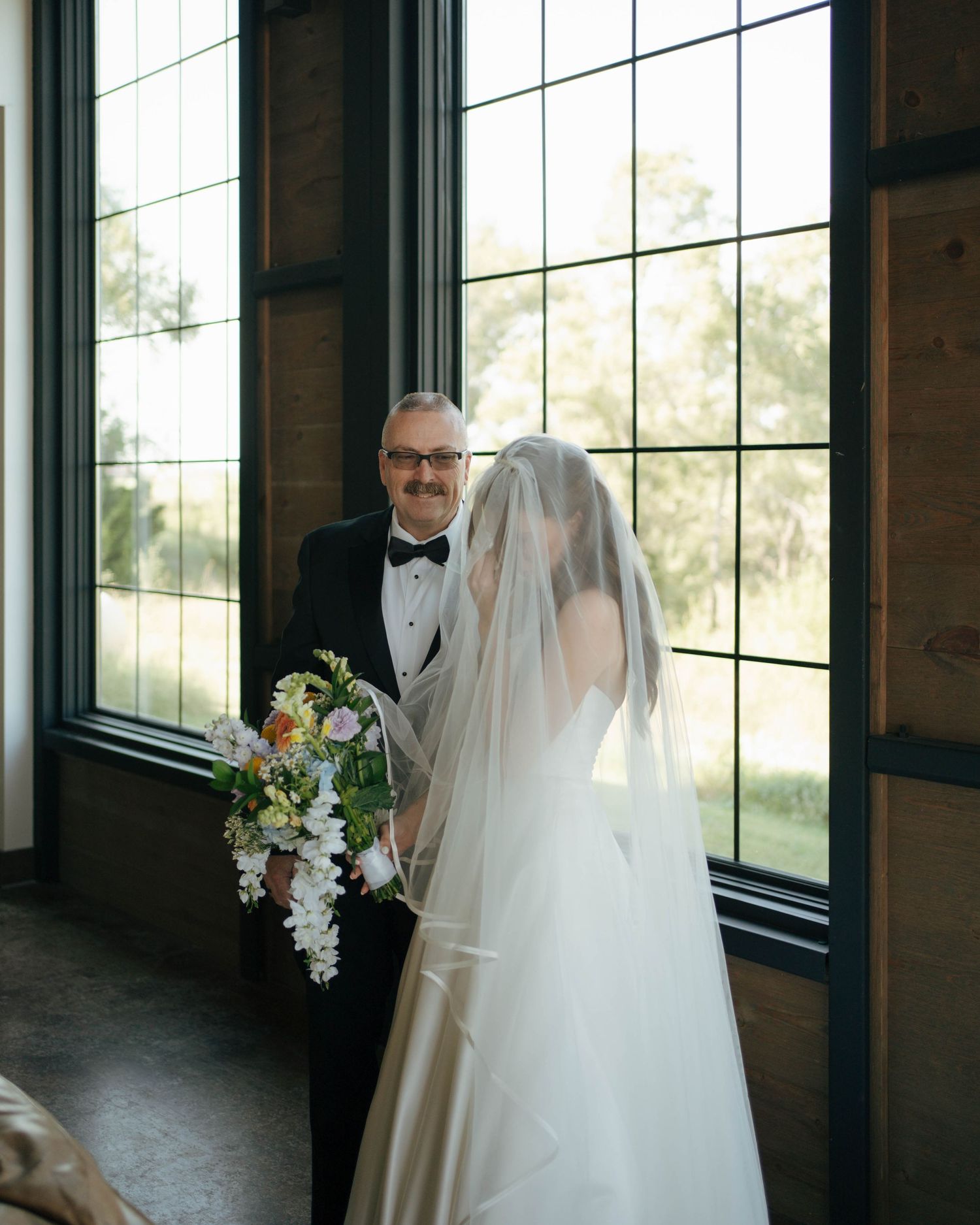 An elegant wedding scene with sunlit windows and a flowing white bridal veil in a rustic indoor setting.