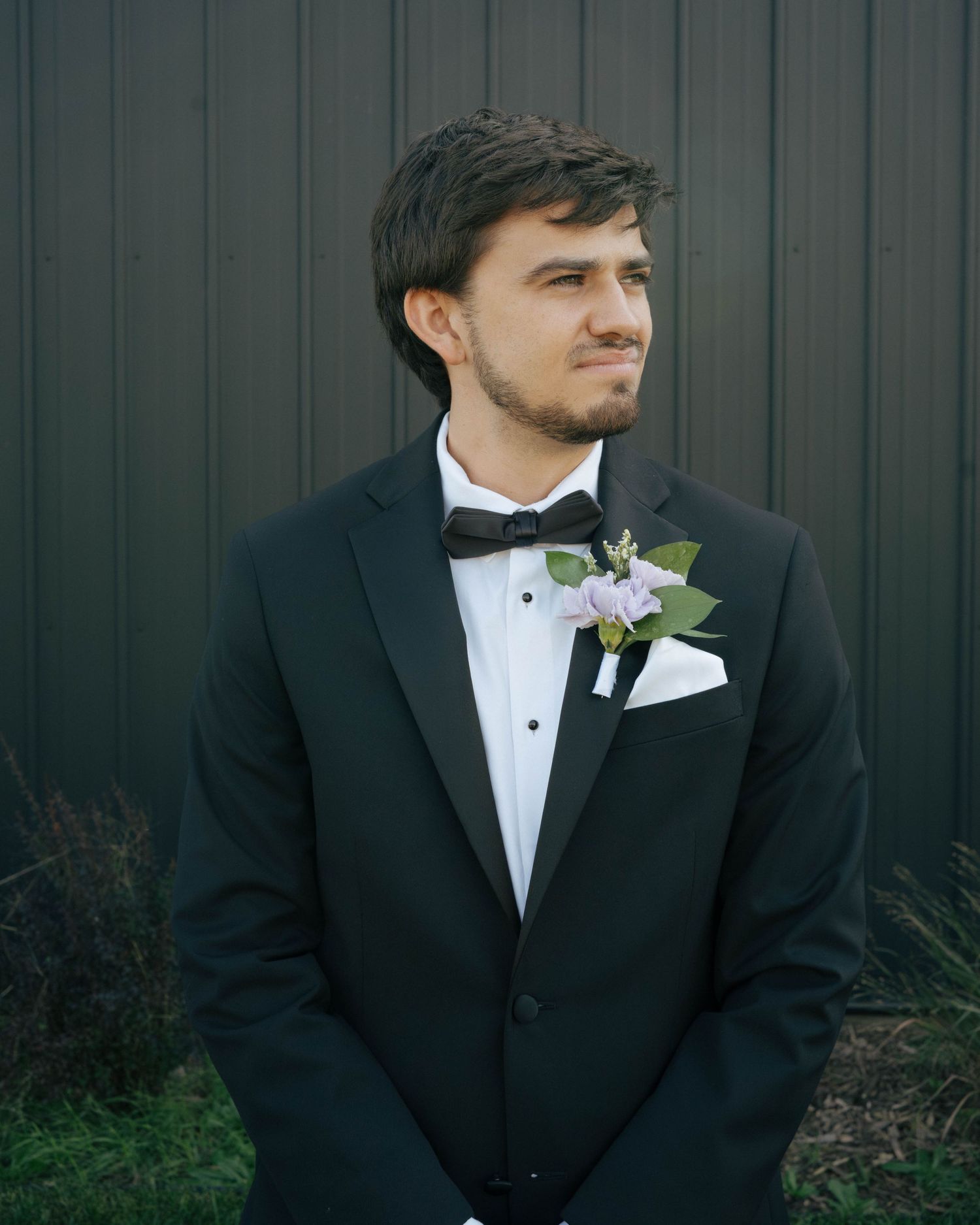 A formal black tuxedo with white boutonniere photographed against a dark wall.