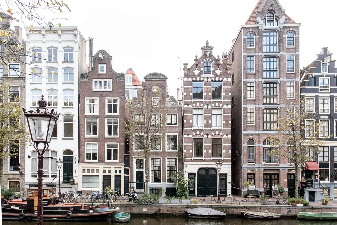 Classic Amsterdam canal lined with tall narrow houses and boats moored along the water.