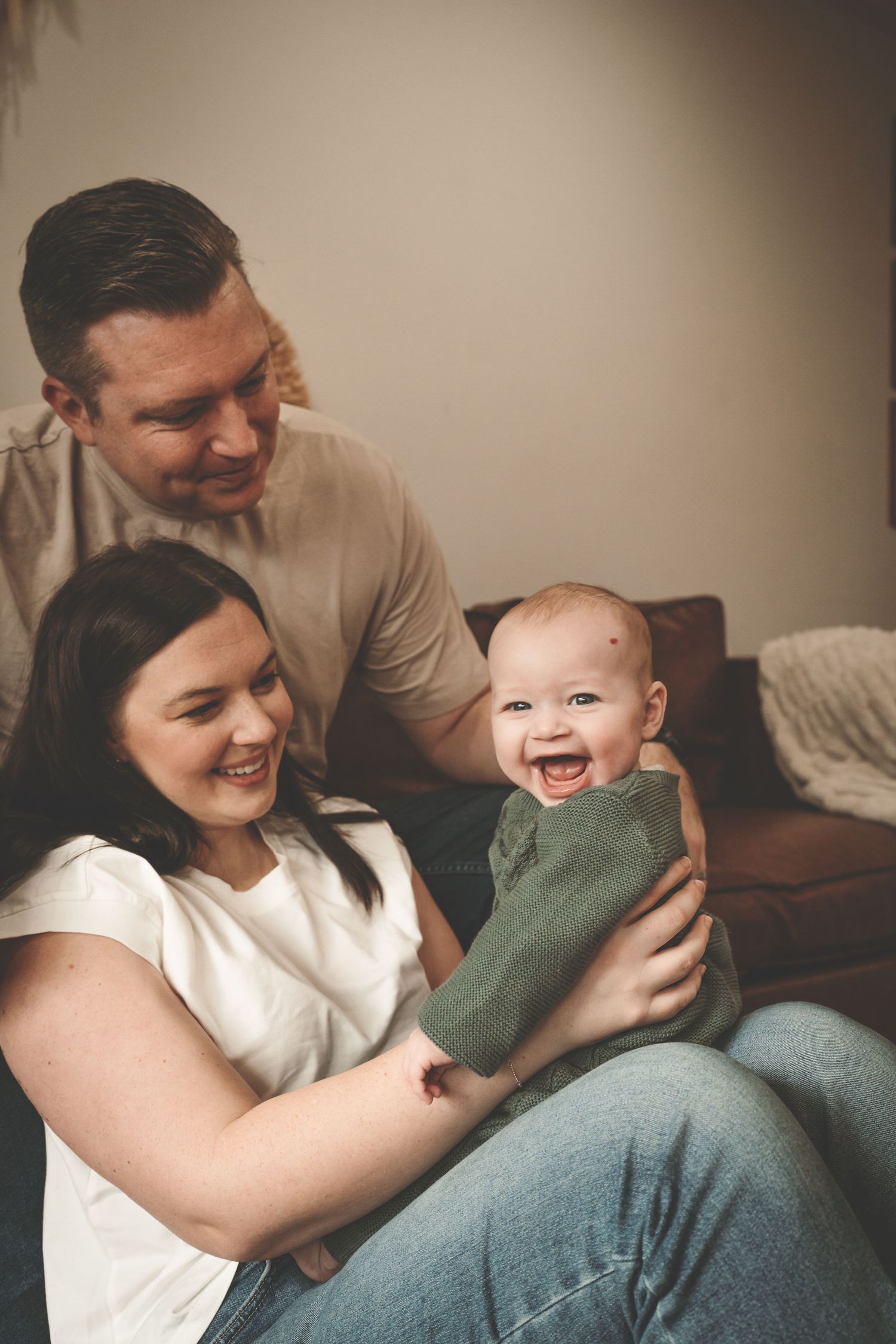 Parents share joyful moments playing with their baby on a couch in warm indoor lighting at lifestyle family session in Arlington Heights