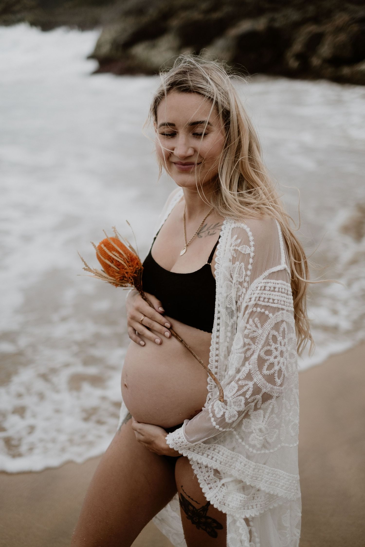 A series of maternity photos showing a woman in a black swimsuit and white lace cover up posing on a beach.