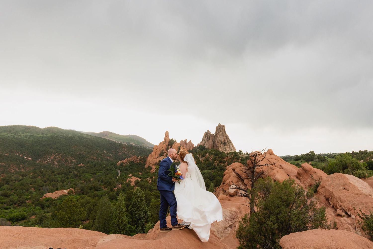 A couple poses on top of a red rock formation at Garden of the Gods in Colorado during their wedding photoshoot.