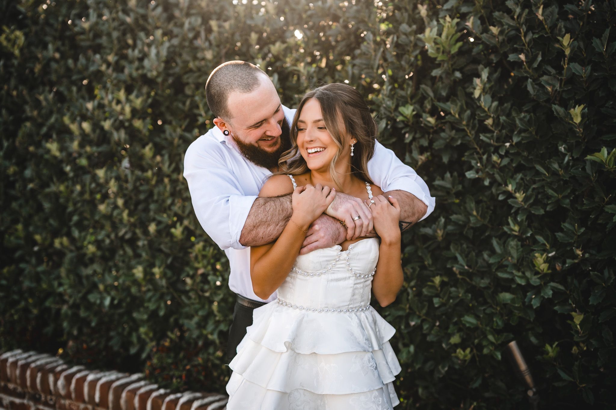 Romantic outdoor engagement photoshoot with couple embracing in sunlit garden setting.