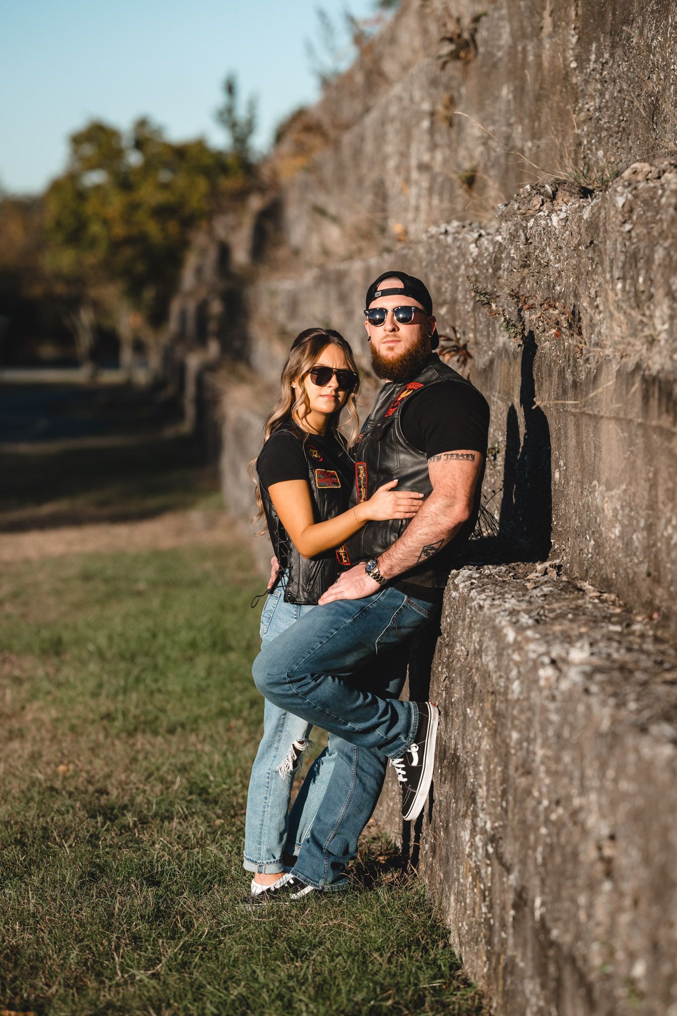 Couple poses against concrete wall during outdoor photoshoot.