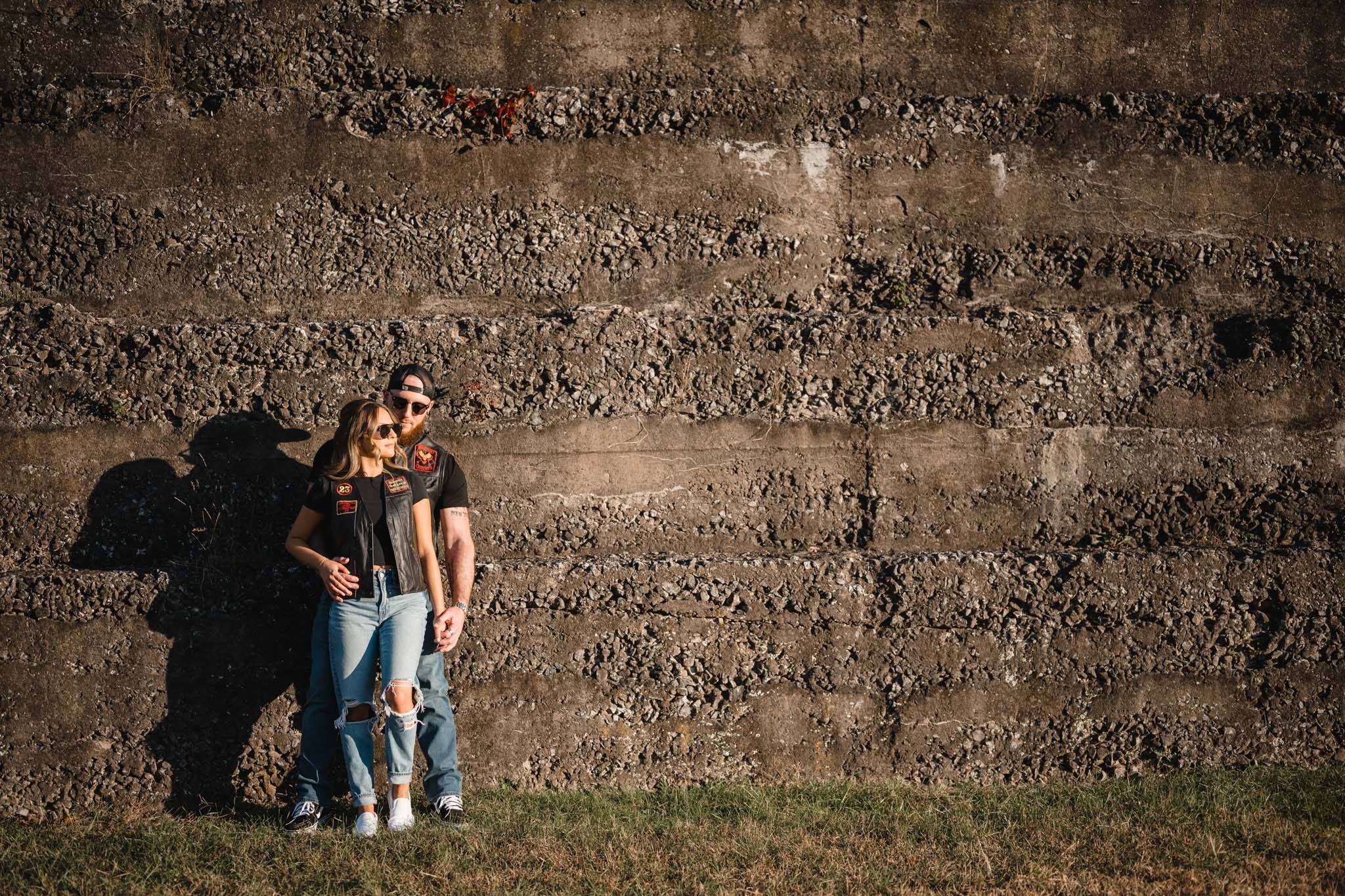 Romantic couple leaning against textured concrete wall in outdoor setting.