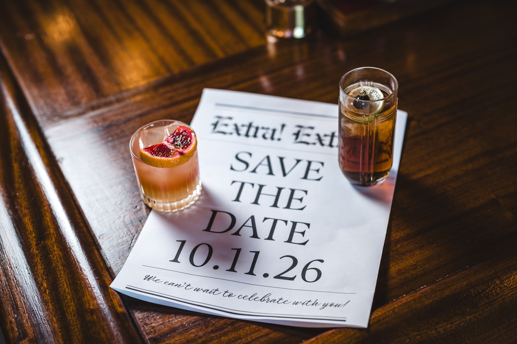 Save the date cards displayed with cocktails on wooden bar surface.