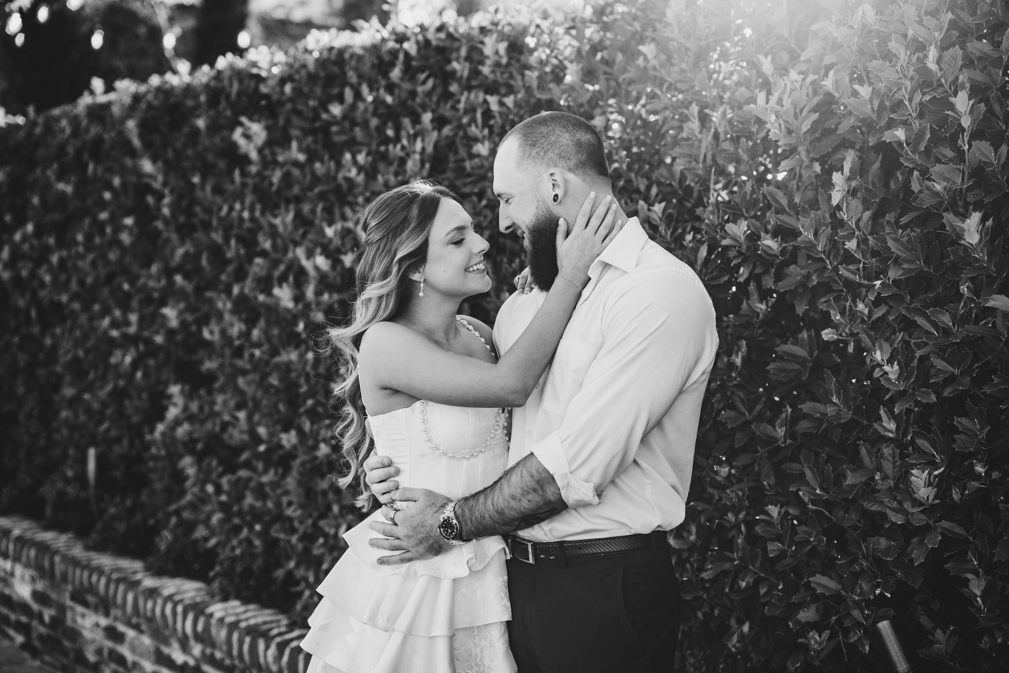 Black and white photo of romantic couple sharing intimate moment among foliage.