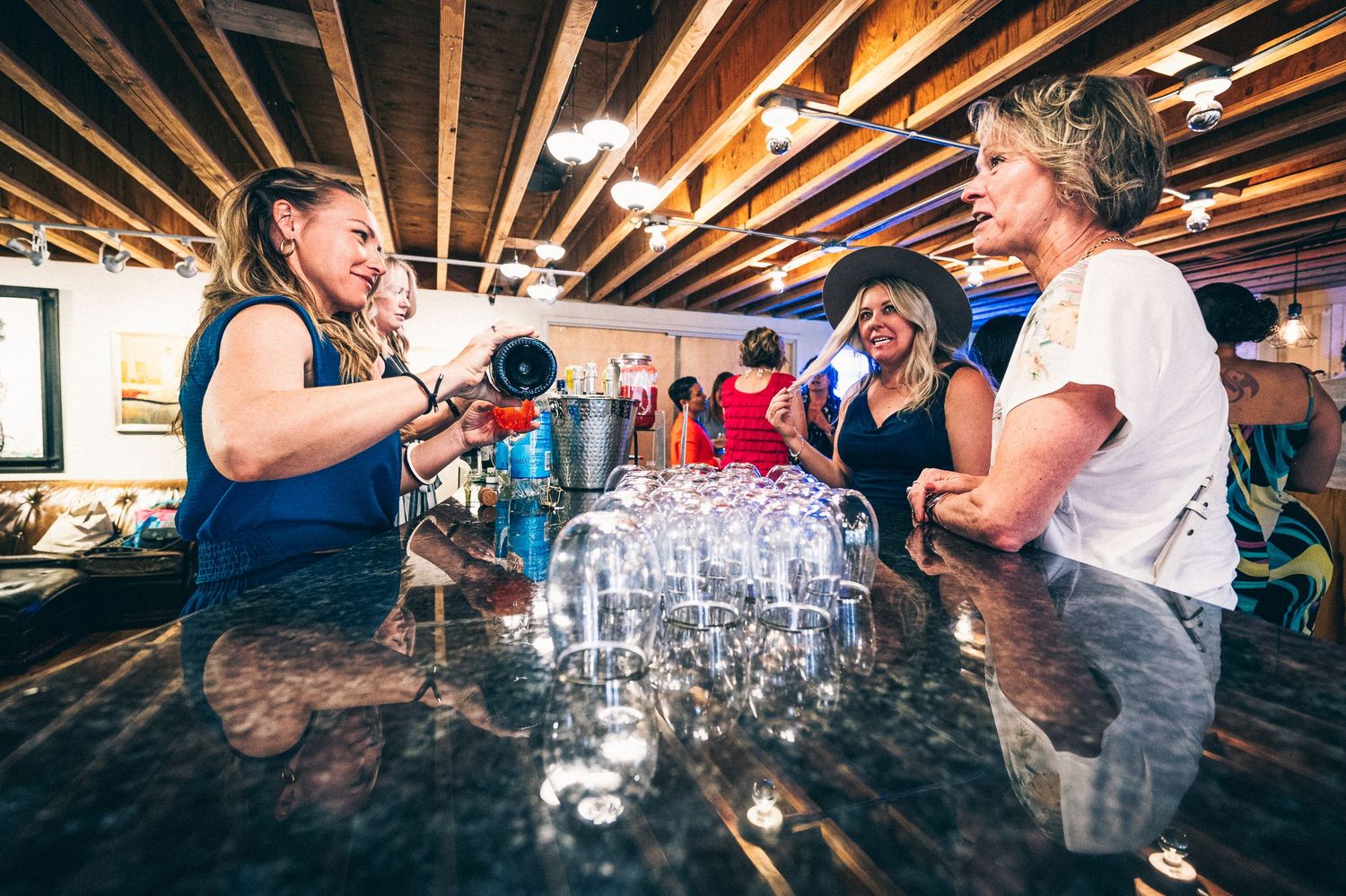 People drinking shots and having fun at a rustic bar counter with wooden beams overhead.