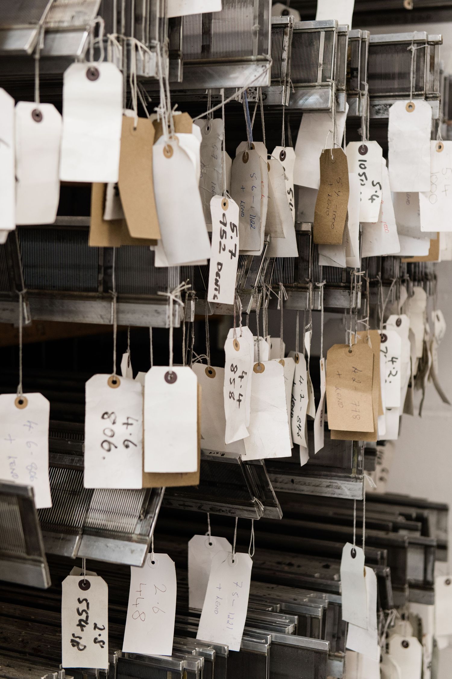 Multiple white paper tags with numbers and text hanging from strings in textile mill