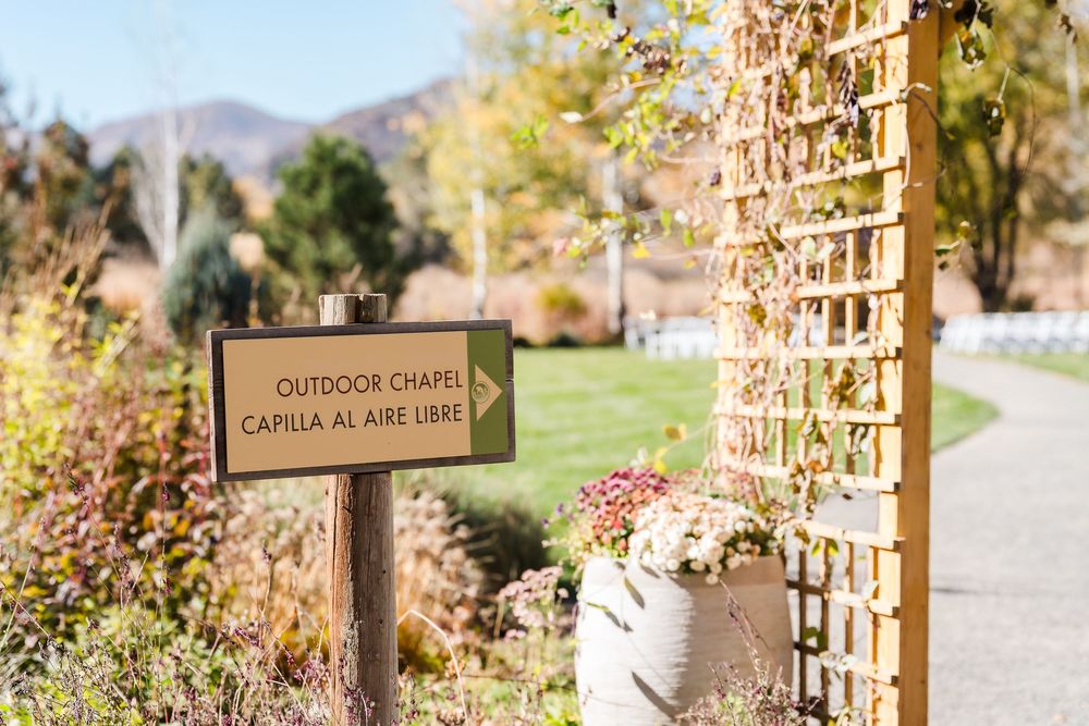 Wooden garden trellis with climbing vines and signage in a tranquil outdoor setting during autumn.