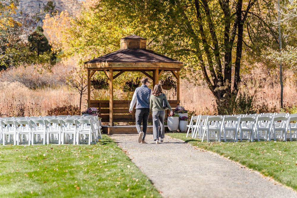 Panoramic view of an outdoor wedding ceremony setup with white chairs and wooden gazebo surrounded by autumn trees.