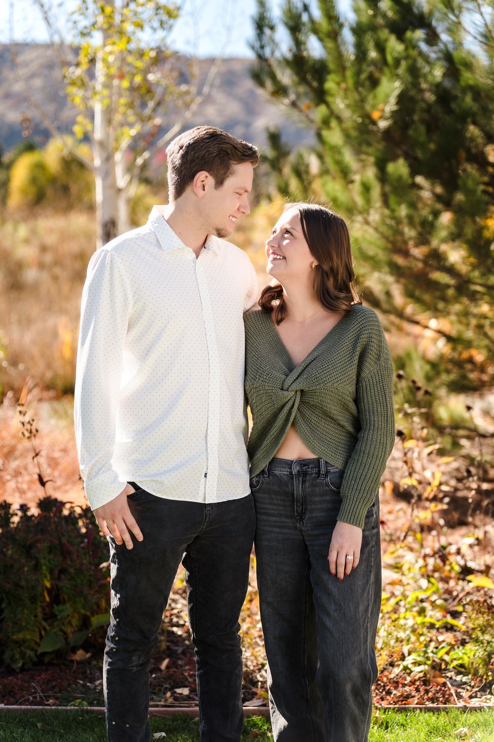 A couple shares a romantic moment together in a park setting with autumn foliage in the background.