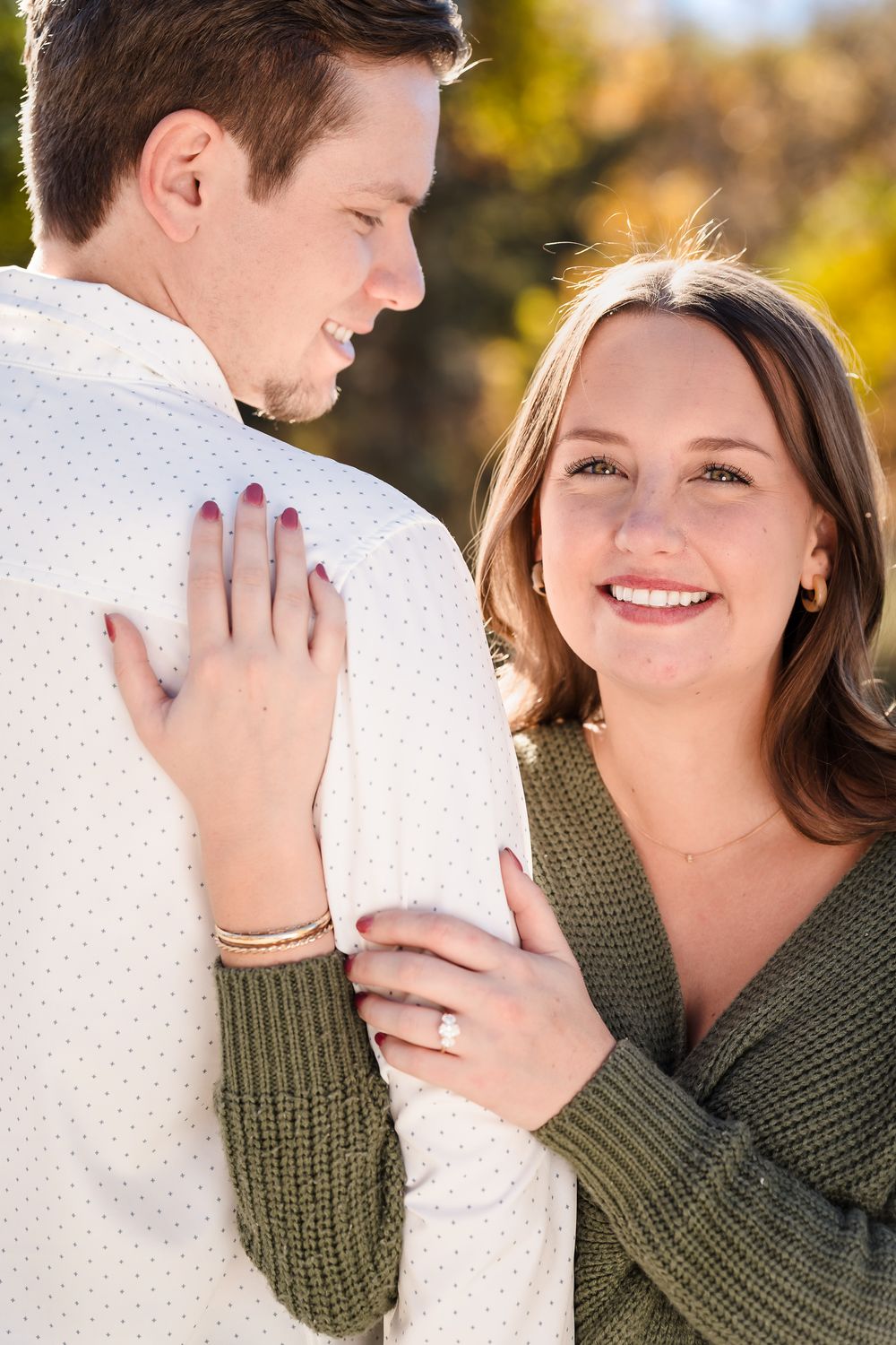 A couple shares tender moments outdoors with fall foliage in the background.