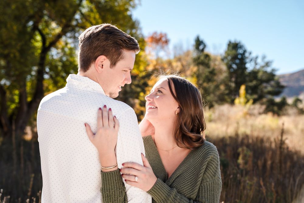 A couple in casual attire shares a romantic moment outdoors during golden hour in a natural setting.