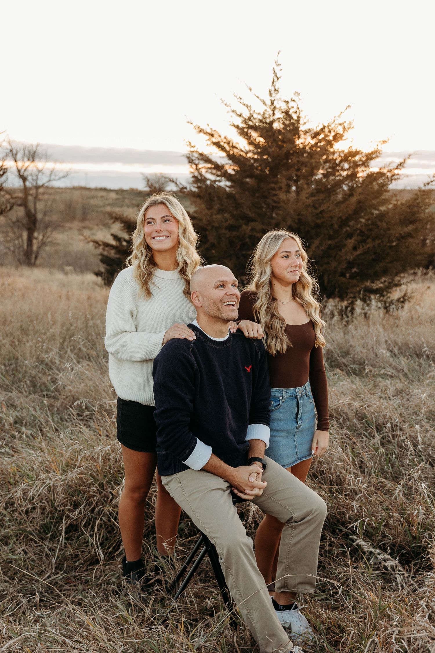 A family sits together in a grassy field at sunset enjoying a candid moment together.