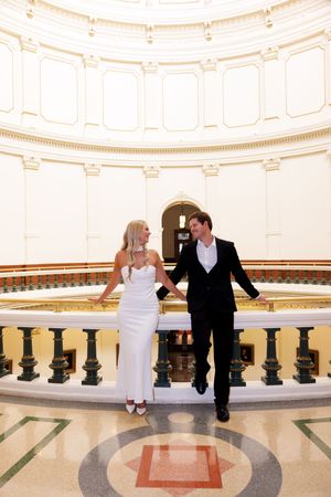 A couple sits together on a curved marble railing in a grand circular hall.