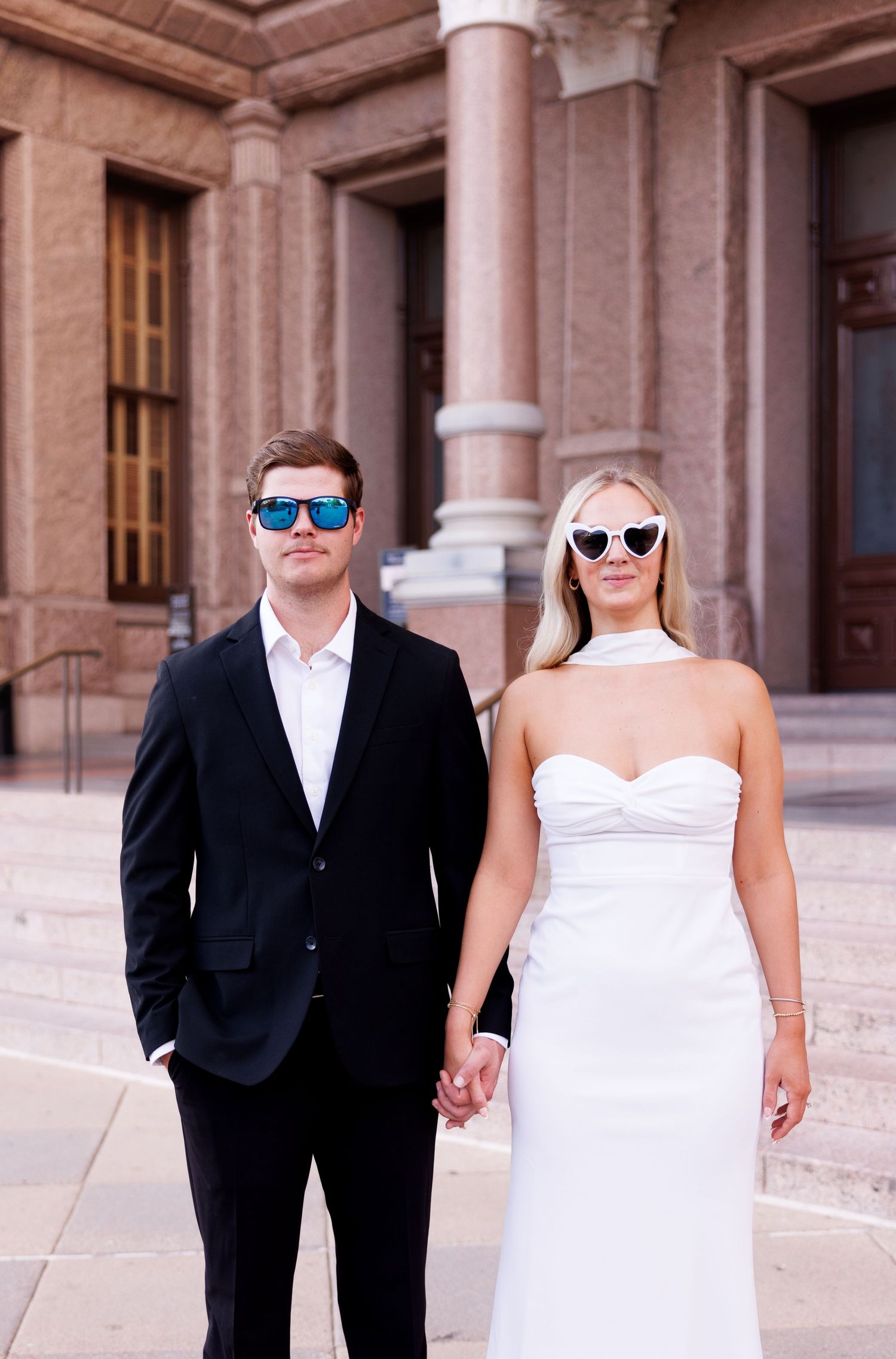 Couple wearing sunglasses poses outside historic building.