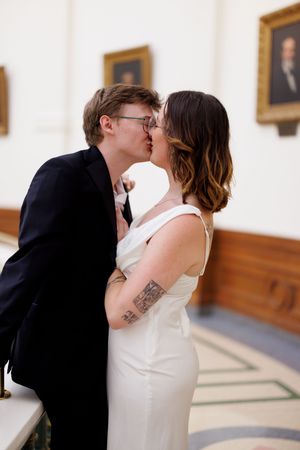 A romantic couple shares an intimate moment in an elegant hallway with wooden paneling and portrait paintings.