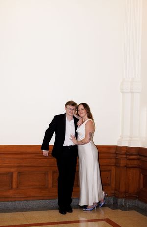A couple shares tender moments along a wooden paneled wall in a formal setting.