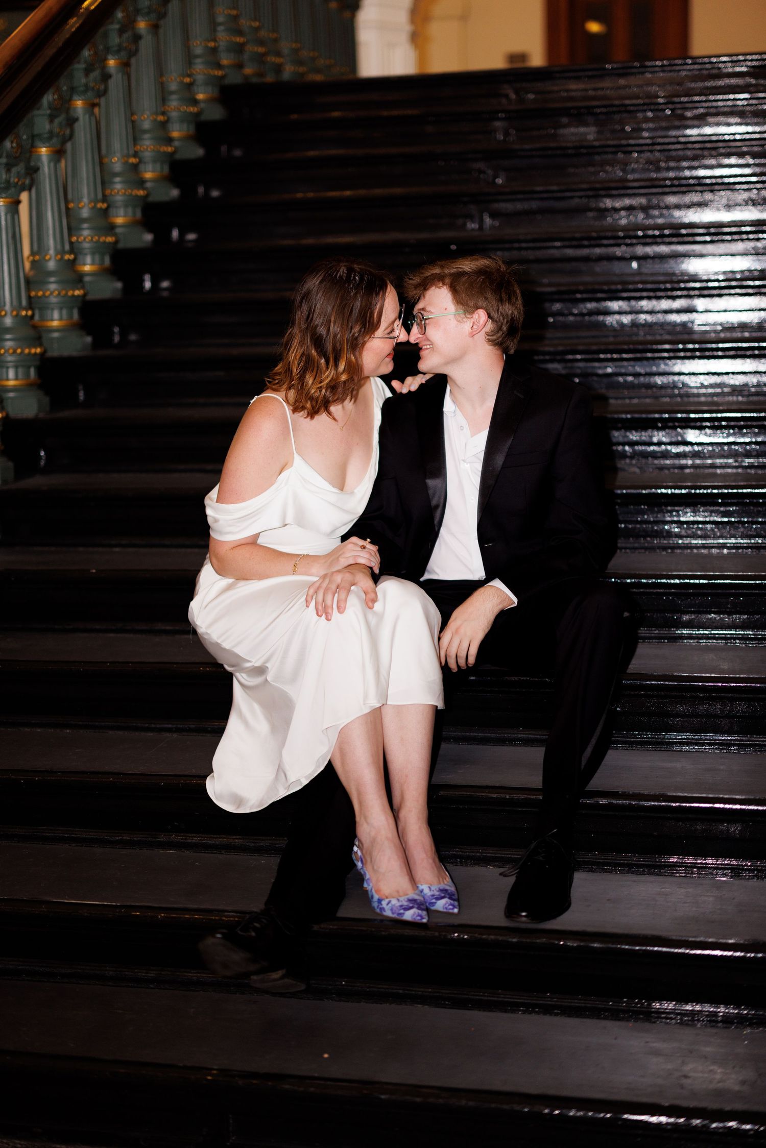 A couple shares romantic moments on dark wooden stairs in dramatic lighting.