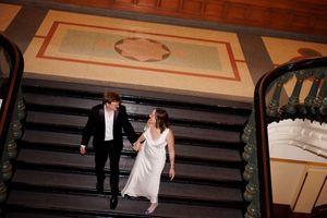 A couple descends an elegant staircase with ornate details and patterned flooring.