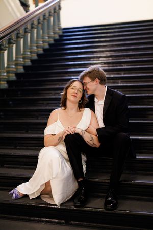 A couple shares intimate moments while seated on grand wooden stairs in dramatic lighting.