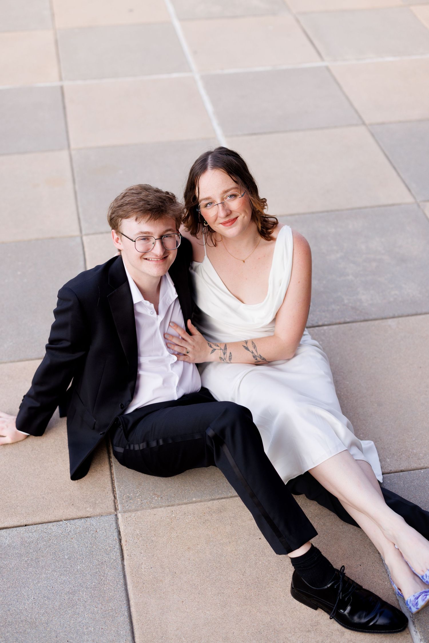 A couple relaxes on stone pavement during an outdoor photo shoot.