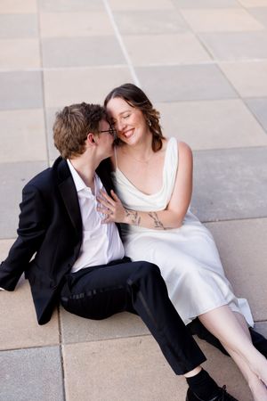 A couple shares an intimate moment while sitting on stone pavement during a photo session.