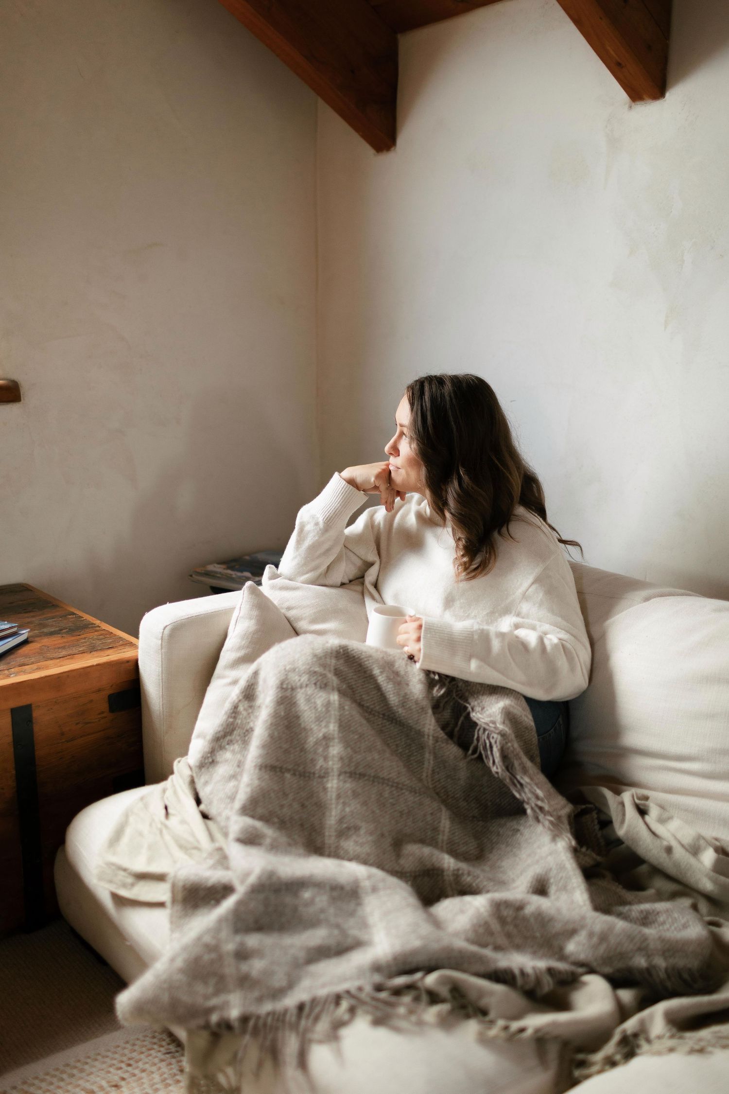A series of photos showing someone relaxing in bed with white linens and a cozy blanket in a rustic room with wooden beams.