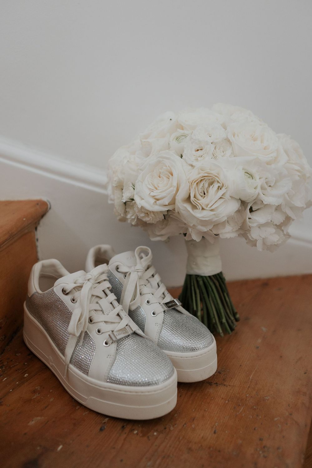 Silver glitter platform sneakers beside a white rose bridal bouquet on wooden staircase steps.