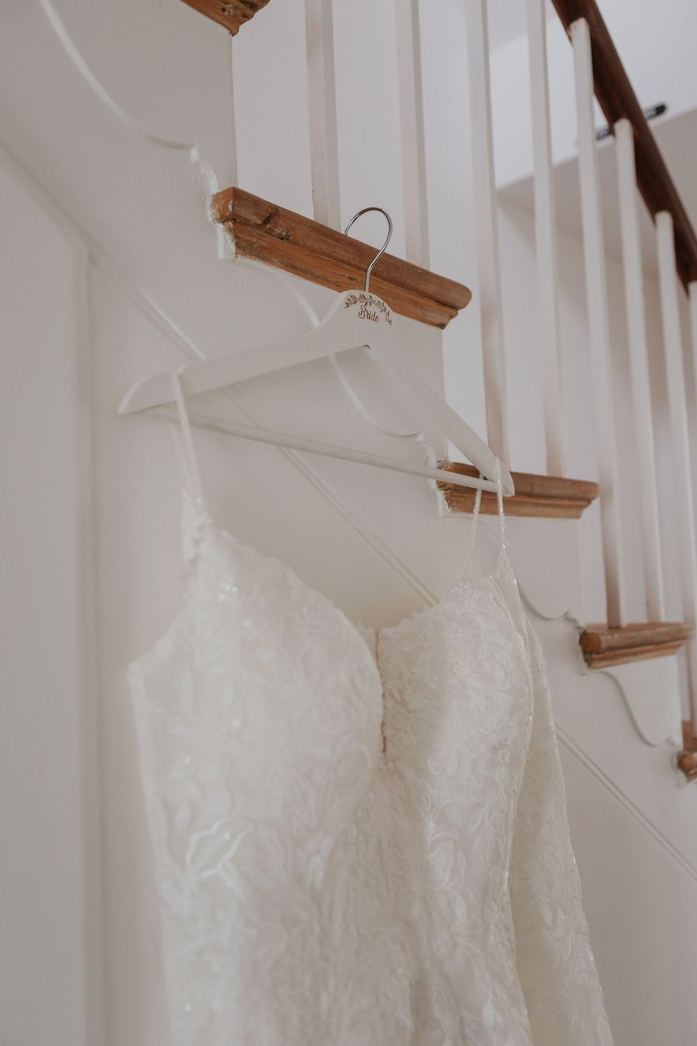 Two white lace wedding dresses hanging on wooden hangers along a staircase banister.