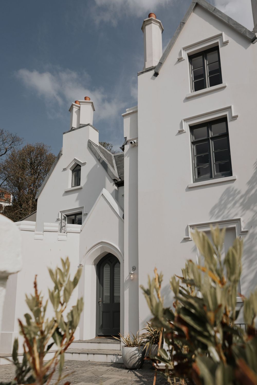 White rendered Victorian house with Gothic arched doorway, chimney stacks and blue sky background.