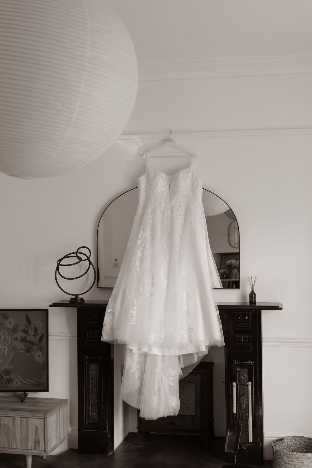White lace wedding dress hanging from a fireplace mantel in a black and white interior photo.
