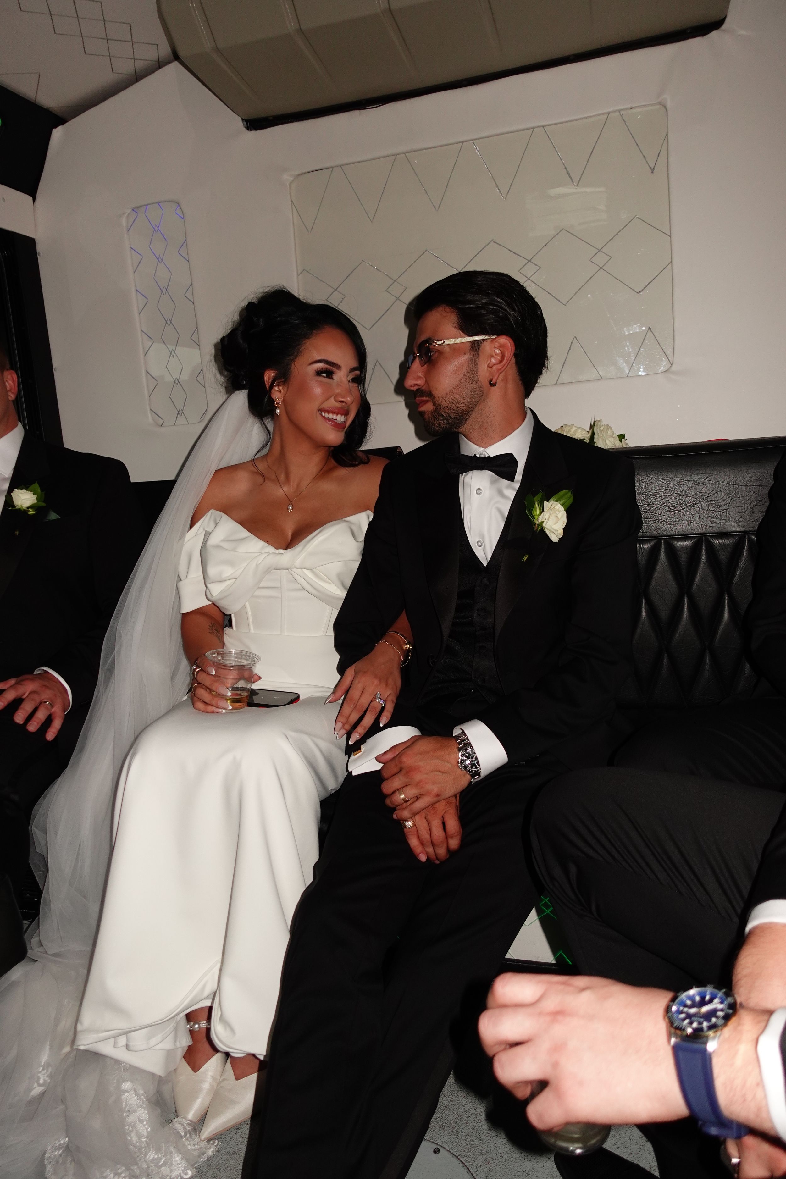 A couple in wedding attire share an intimate moment while seated together on a black leather couch.