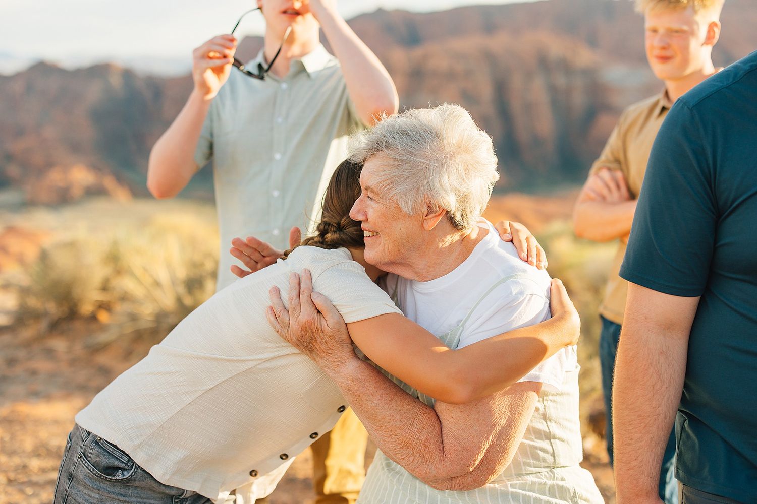 A family shares tender moments together against a backdrop of red desert cliffs at sunset.