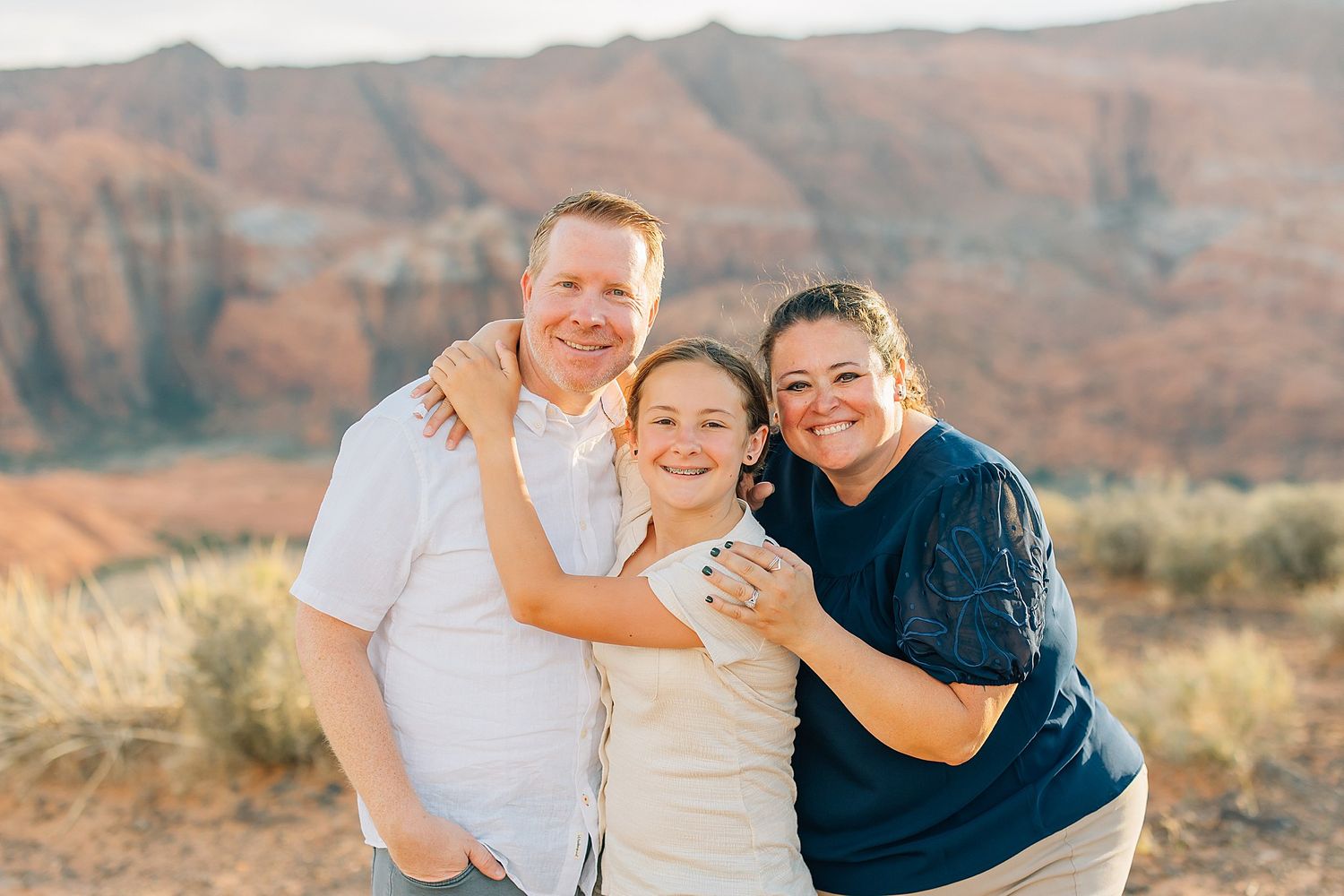 Family embracing and laughing together on a desert overlook with red rock mountains in the background.
