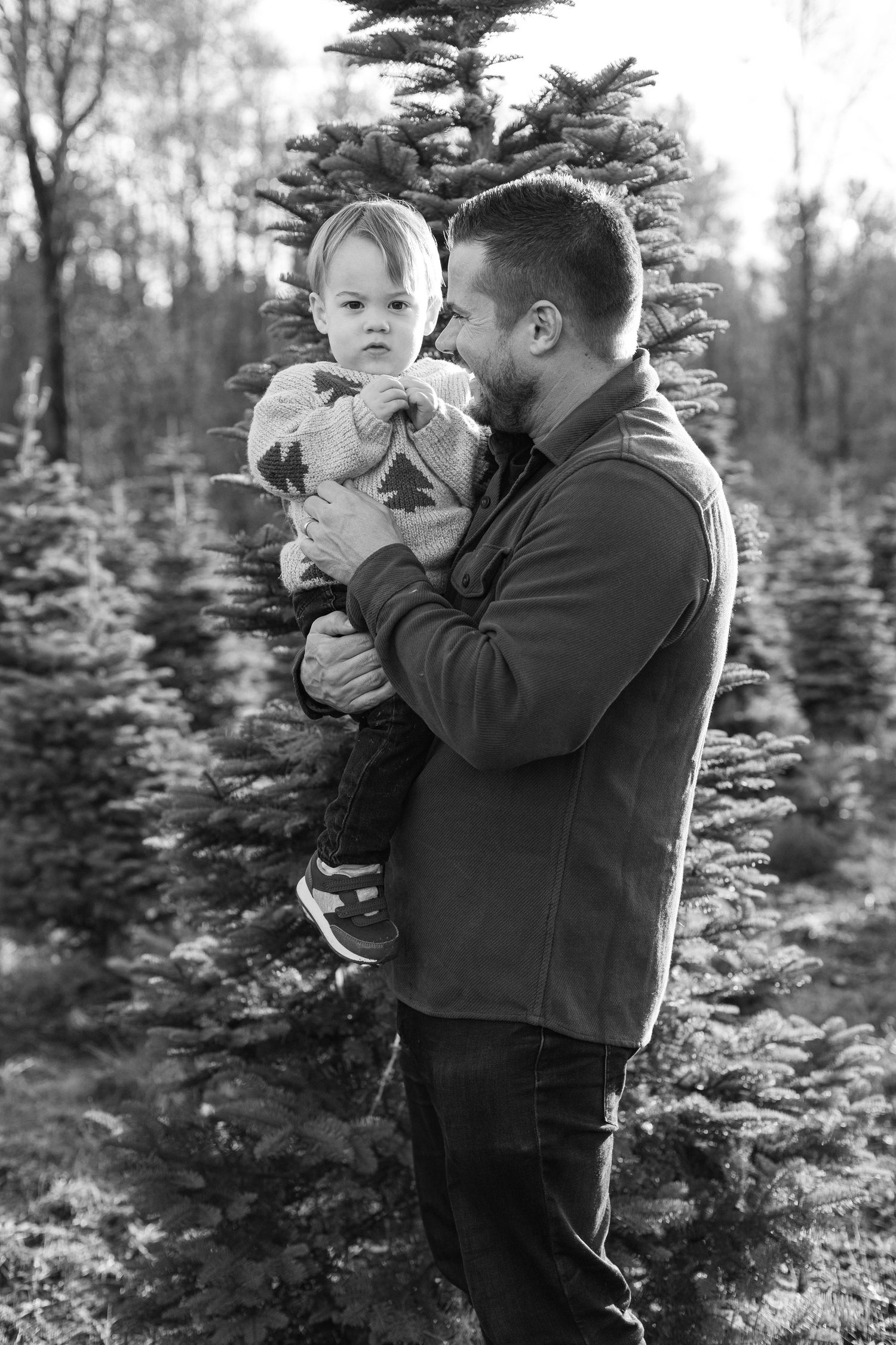 Black and white series of candid moments between parent and child among evergreen trees at a Christmas tree farm.