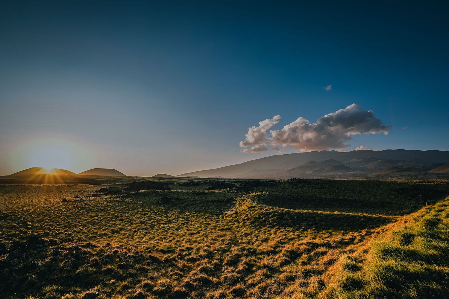 A dramatic panoramic landscape with rolling green hills and a golden sunset illuminating clouds over the horizon.