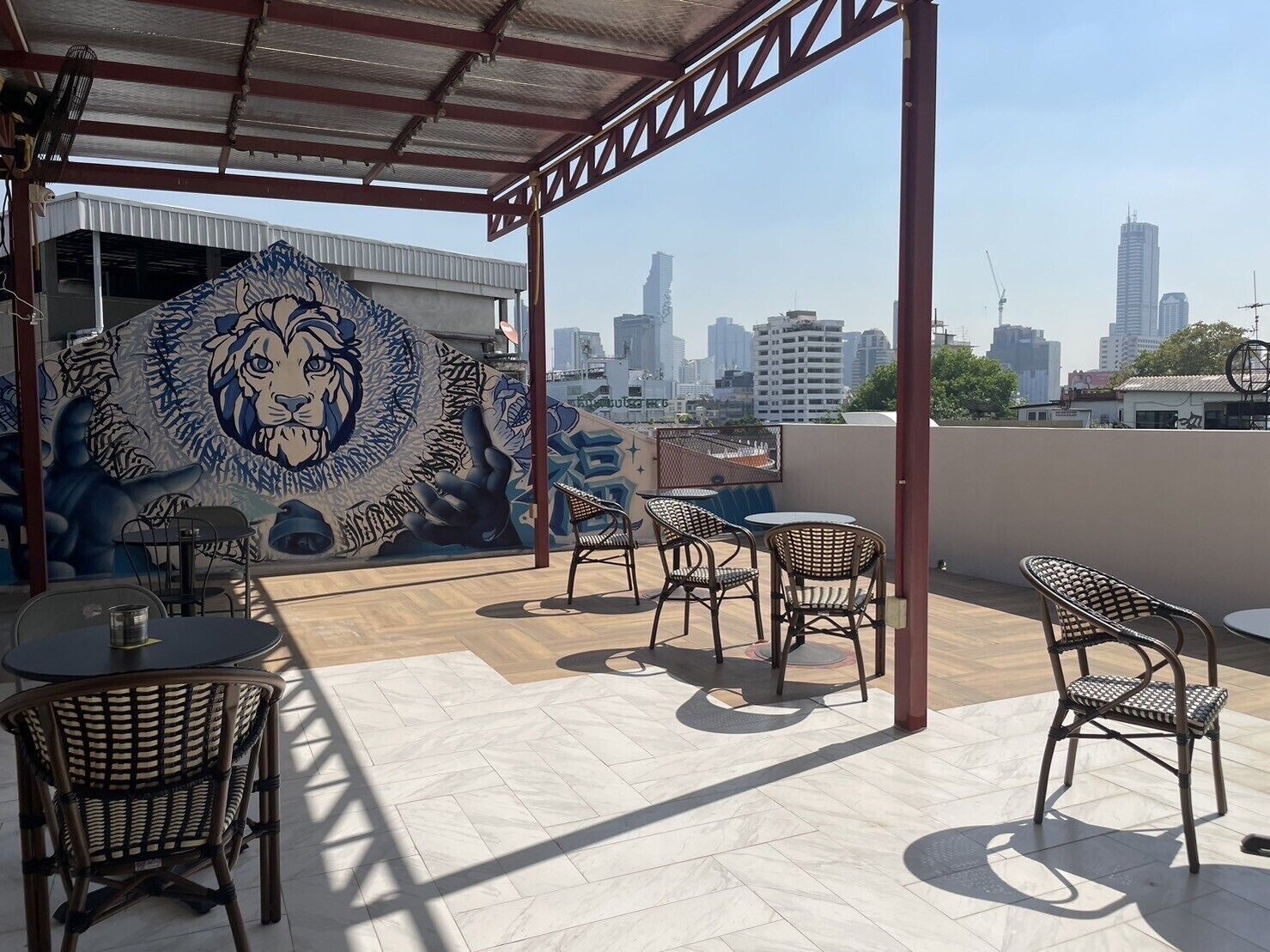 Covered outdoor patio seating area with black metal chairs overlooking a city skyline view.